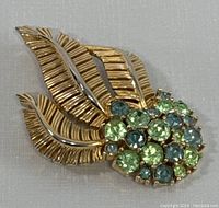 Front view showing gilded leaves with textured details and cluster of green and blue rhinestones.
