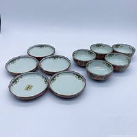 10 small Arita ware bowls with scalloped edges, white interior with green and gold floral detail, and red and blue geometric pattern exterior with gold accents.