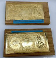 Two gold-plated 10000 yen replicas on wooden stands with blue measuring ruler