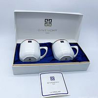 Two white porcelain mugs with Givenchy logo displayed in blue fabric-lined box with Givenchy branding and certificate card.