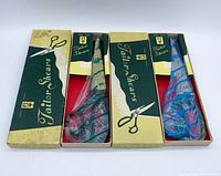 Two sets of Japanese tailor scissors in original boxes with printed labeling 'Tailor Shears'. One pair in green packaging, one in blue.