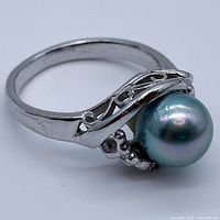 Close-up side angle of silver ring showing bluish-grey genuine pearl and ornate design on band.
