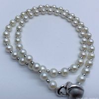 Close-up image showing the round white Akoya pearls and silver beads, as well as silver clasp with heart detail.