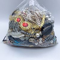 Full view of plastic bag filled with mixed costume and vintage jewelry including pearl-like necklaces, gold-tone and silver-tone pieces.