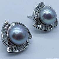 Close-up angled view of the pair of cobalt gray genuine pearl earrings showing the front, highlighting the pearl size and baguette clear stones on silver-tone frame.