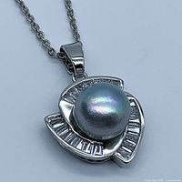 Front view of the genuine grey pearl pendant with silver tone setting and baguette-cut clear stones around the pearl on silver chain.