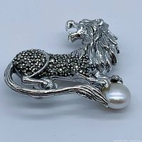 Close-up side view of lion brooch with pearl and marcasite gemstones.