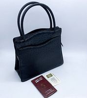 Front angle of handbag with certification booklet and card laid in front