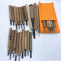Top-down photo showing entire lot of assorted Japanese carving tools with wooden handles and an orange pouch containing smaller tools.