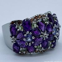 Close-up angled view of multi-gemstone sterling silver ring showing amethyst, peridot, and tanzanite stones clustered in floral design with orange accent stones.