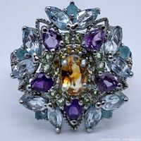 Front view of multi-gemstone ring showing oval citrine center with surrounding amethyst, aquamarine, and peridot stones in 925 silver with white gold plating.