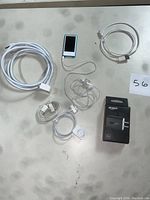 Lot contents including blue iPod Nano, headphones, USB cables, Amazon 9W charger in box, and iMac desktop power cord on grey surface.