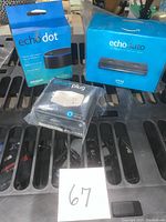 Photo shows unopened boxed Amazon Echo Dot, Echo Auto, and Smart Plug placed on black slatted surface.