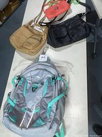 Photo of four bags on a table showing High Sierra backpack, Guess clutch, and two additional handbags in tan and black worn condition.