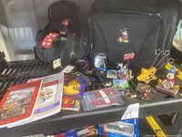Full view of lot showing both Disney camera bags, collectible pins, books, keychains, calculators, and 100th anniversary Mickey decoration.