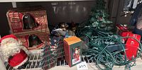 Photo showing the full assortment of holiday items: two boxed sets of holiday tumblers, metal candle holders shaped like Christmas trees, ceramic tree, assorted figurines, string lights, and vintage plush Santa.