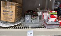 Wide shelf view showing boxed 9-piece Anchor Hocking caddy set, clear glass caddy, sleigh candy bowl, CDs stacked, and holiday candy jars.