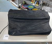 Black vinyl dust cover for the IBM Selectric II typewriter placed on white table with shelves in background.