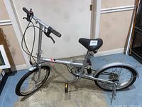 Full side view of the silver Komda folding bike showing frame, seat, wheels, and handlebars