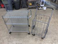 Metal rolling shop cart with three wire mesh shelves alongside collapsible rolling grocery cart with wire basket and handle.