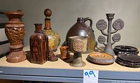 Full view of all items showing a variety of vessels, candle holders and folk art pieces on a shelf.