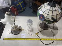 Photo showing both lamps and the crystal vase on a white table surface with measuring tape.