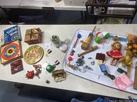 Wide view of assorted vintage wooden toys, puzzles, marbles, metal Jax pieces, vintage dolls, coin purses, 1968 Hot Wheels car, 1960s Mattel spinning tops on white table.