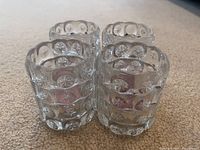 Photo showing four clear glass candle or tea light holders on carpet background, highlighting their circular etched and star pattern.