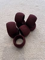Eight brown napkin rings wrapped in textured fabric placed on a light carpeted floor