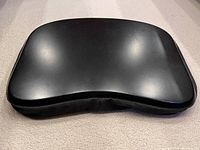 Photo of a black laptop cushion with a contoured shape, showing the smooth padded surface.