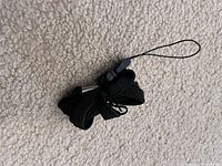 Photo of a coiled black fabric lanyard with a plastic slider and a thin tie-on loop attachment, placed on a textured beige surface.