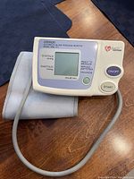 Photo of Omron automatic blood pressure monitor model HEM 711 with cuff on wooden surface.