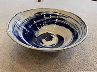 Photo of a round ceramic bowl featuring a blue and white swirl pattern inside, showing the bowl from an angled top view on a carpeted surface.