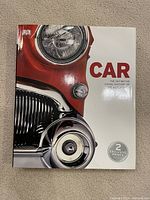 Cover of the new coffee table book titled 'Car The Definitive Visual History of the Automobile' showing a classic red car headlight and grille.