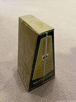 View of the metronome box standing upright on a surface, showing the worn green and beige box with volume and tone markings on the side.