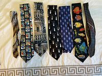 Seven men's neck ties arranged horizontally on a light-colored background showing various colorful and patterned designs.