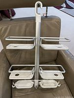 Front view of metal shower organizer showing four shelves with drainage holes,  multiple hooks, and large white hanging hook.