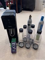 Photo showing SodaStream soda maker unit, 5 reusable bottles, 2 bubly flavoring bottles, full CO2 canister and empty CO2 canister