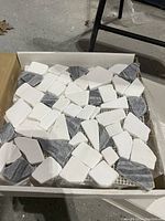 Top view of 12 pebble tile sheets showing mixed white and black smooth pebbles attached on mesh backing.