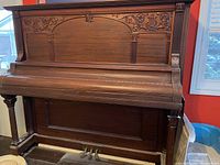 Front view of the upright piano showing carved floral designs and wood finish.