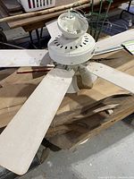 White ceiling fan with five attached blades, showing motor housing and mounting components on a wooden surface.