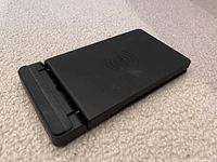 Folded flat view of a black wireless charger showing charging area and base hinge.