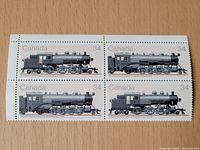 Front view of four Canada 34 cent railroad stamps featuring different steam locomotives placed on a wooden surface.