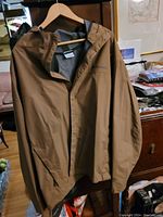 Brown Columbia men's rain jacket hanging on a wooden hanger showing full front side with hood and zipper.