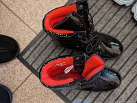 Top view showing the shiny black patent material, red inner lining, lace-up front, and side zipper of the boots.