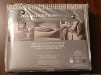 Photo of Gluckstein Home branded packaging showing the 3-piece queen duvet cover set with beige and white geometric pattern, 100% cotton, in original packaging.