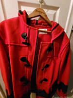 Front view of red blanket coat showing toggle closures and zipper, hanging on hanger.