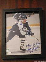 Framed 8x10 color photograph of Lanny McDonald in Toronto Maple Leafs uniform skating on ice, signed with inscription in blue ink on lower right corner, visible hologram sticker on bottom left of photo.