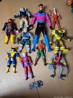 Top-down image showing all 10 X-Men figures laid out on a wooden surface, displaying various poses and sizes