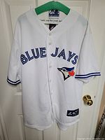 Front view of white Toronto Blue Jays Majestic baseball jersey hanging on green hanger, showing 'BLUE JAYS' text and team logo on chest.